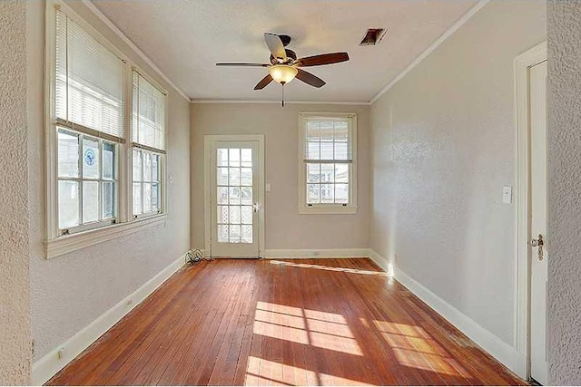 doorway featuring wood-type flooring, visible vents, crown molding, and baseboards