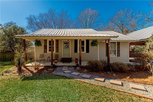 view of front facade with a porch, metal roof, fence, and a front lawn