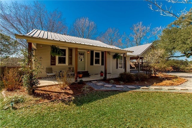 ranch-style home featuring covered porch, fence, metal roof, and a front yard