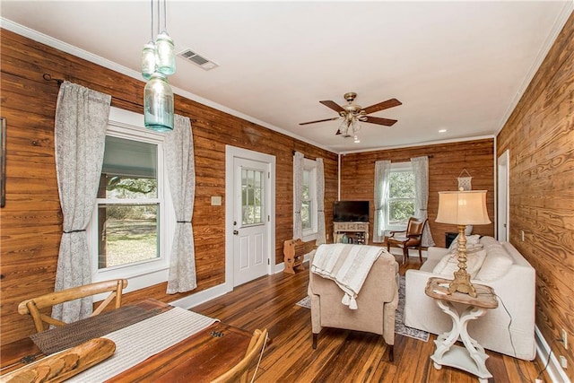 living area featuring ceiling fan, wood walls, dark wood-style flooring, visible vents, and crown molding