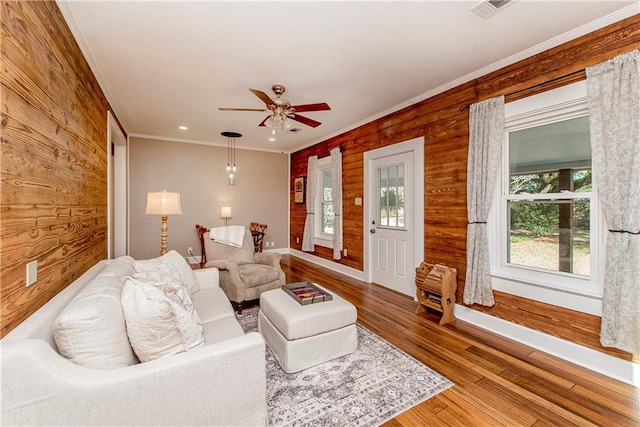 living area featuring visible vents, a ceiling fan, ornamental molding, wood finished floors, and wood walls