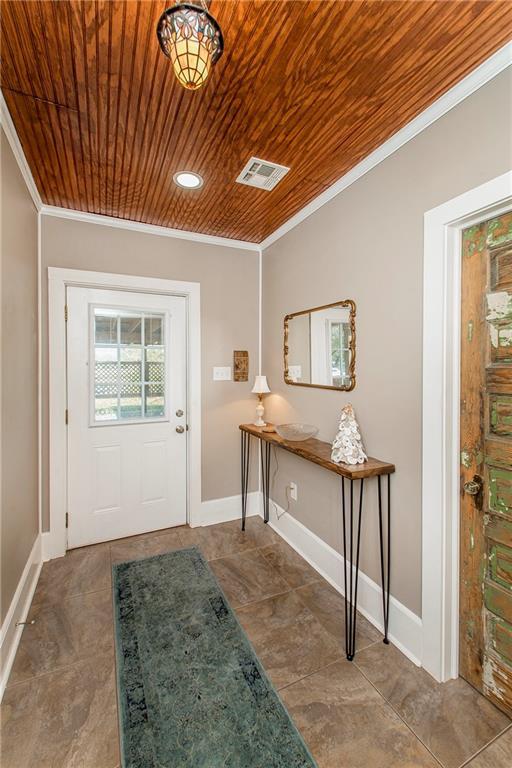 doorway to outside with baseboards, wood ceiling, visible vents, and crown molding