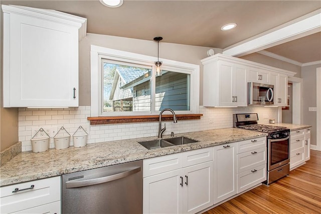 kitchen featuring white cabinets, light stone countertops, stainless steel appliances, light wood-style floors, and a sink