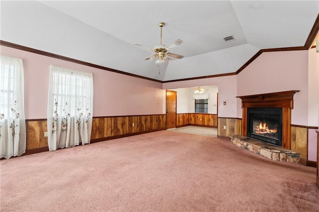 unfurnished living room featuring visible vents, a glass covered fireplace, wainscoting, vaulted ceiling, and wooden walls