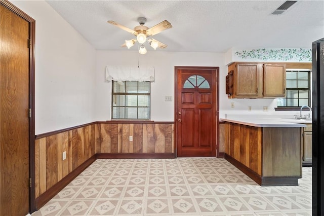 kitchen with a wainscoted wall, light countertops, visible vents, wooden walls, and a peninsula