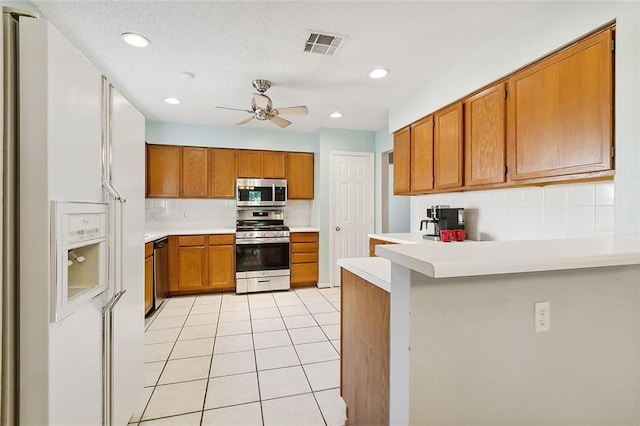 kitchen with a peninsula, visible vents, light countertops, appliances with stainless steel finishes, and brown cabinets