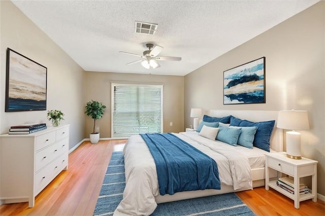 bedroom with baseboards, light wood-style flooring, visible vents, and a textured ceiling