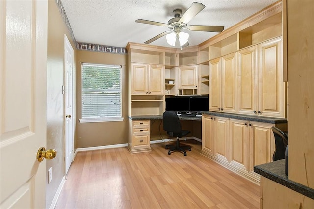 home office with light wood-type flooring, a textured ceiling, baseboards, and built in desk