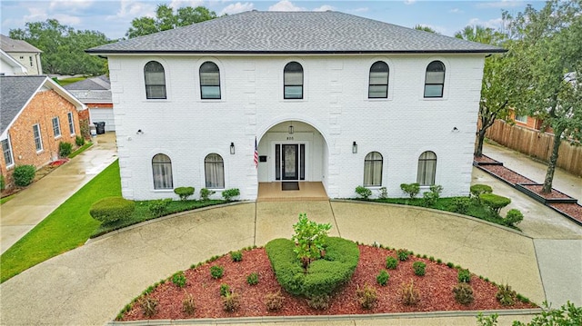 view of front of house featuring roof with shingles, fence, and brick siding