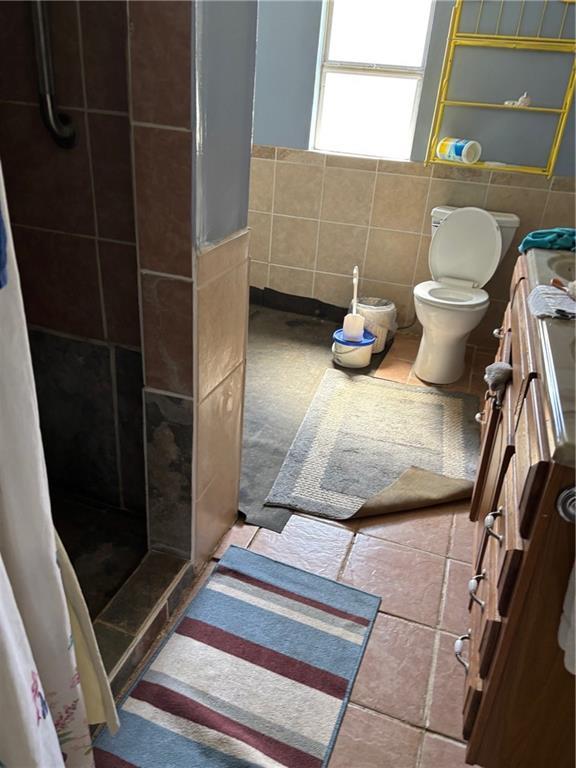 bathroom featuring toilet, a shower stall, tile walls, and tile patterned floors