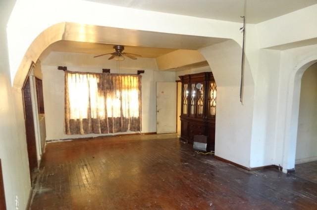 empty room featuring baseboards, wood-type flooring, arched walkways, and a ceiling fan