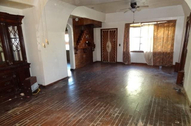 unfurnished living room featuring ceiling fan, arched walkways, and wood finished floors