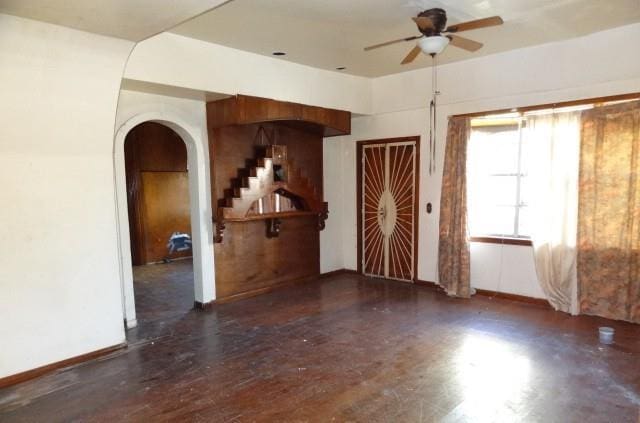 unfurnished room featuring a ceiling fan, arched walkways, baseboards, and stairs