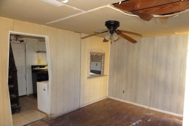 unfurnished room featuring ceiling fan, baseboards, wood finished floors, and wooden walls