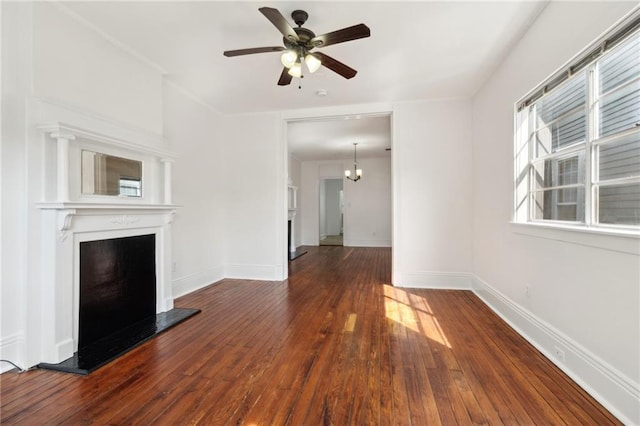 unfurnished living room featuring baseboards, a fireplace with raised hearth, hardwood / wood-style floors, and ceiling fan with notable chandelier