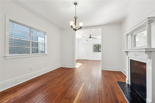 unfurnished living room featuring baseboards, hardwood / wood-style flooring, a fireplace with flush hearth, crown molding, and ceiling fan with notable chandelier