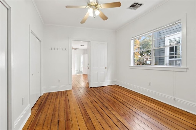 unfurnished bedroom featuring crown molding, a closet, wood-type flooring, visible vents, and baseboards