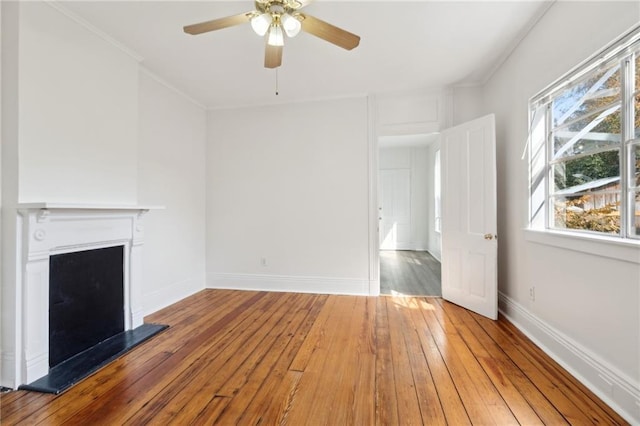 unfurnished living room featuring a fireplace with raised hearth, hardwood / wood-style floors, crown molding, and baseboards