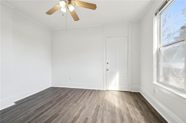 empty room featuring crown molding, dark wood finished floors, baseboards, and ceiling fan