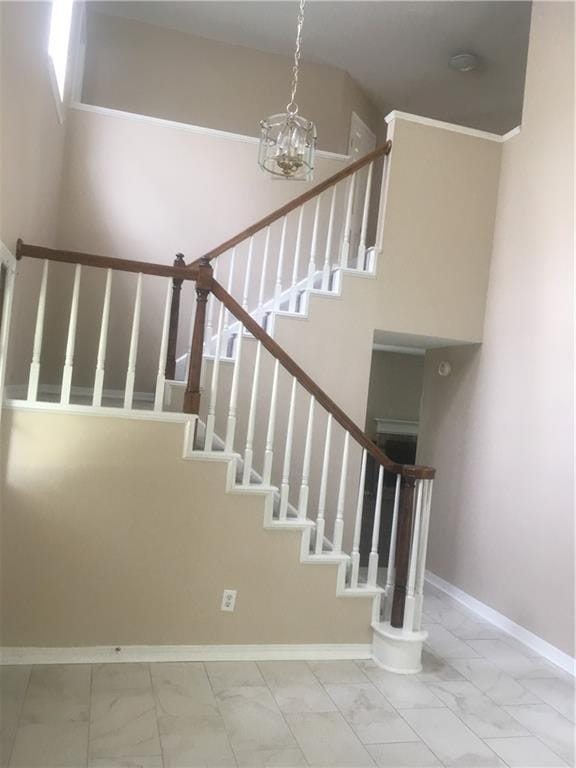 staircase featuring marble finish floor, a high ceiling, an inviting chandelier, and baseboards