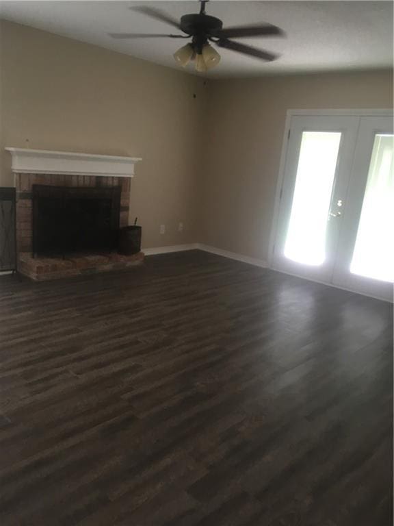 unfurnished living room with a ceiling fan, baseboards, french doors, a brick fireplace, and dark wood-style floors