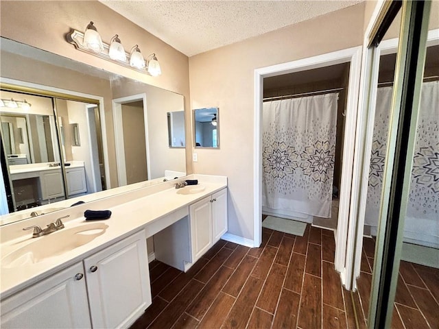 bathroom featuring a textured ceiling, double vanity, a sink, and wood tiled floor