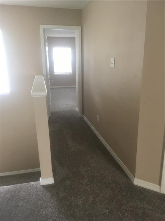 hall featuring baseboards and dark colored carpet