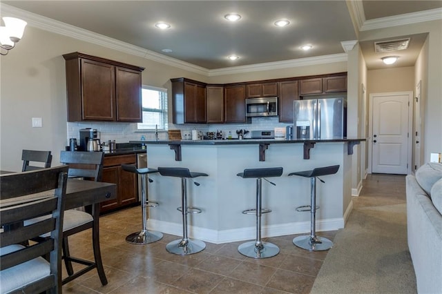 kitchen featuring dark brown cabinetry, visible vents, dark countertops, appliances with stainless steel finishes, and a kitchen breakfast bar