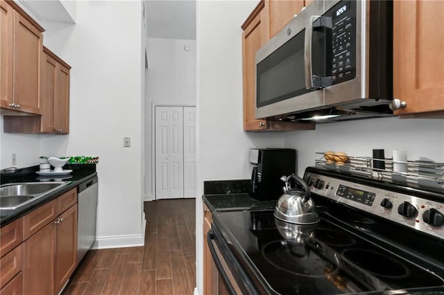 kitchen featuring stainless steel appliances, a sink, baseboards, brown cabinets, and dark wood-style floors