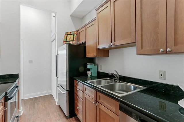 kitchen featuring baseboards, brown cabinetry, light wood-style flooring, stainless steel appliances, and a sink