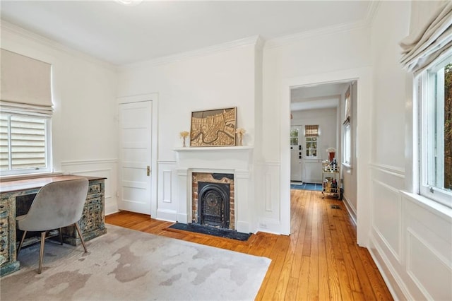 home office featuring a wainscoted wall, a decorative wall, ornamental molding, a fireplace with flush hearth, and hardwood / wood-style floors