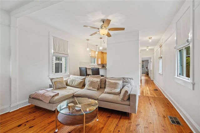 living area with baseboards, a ceiling fan, visible vents, and light wood-style floors