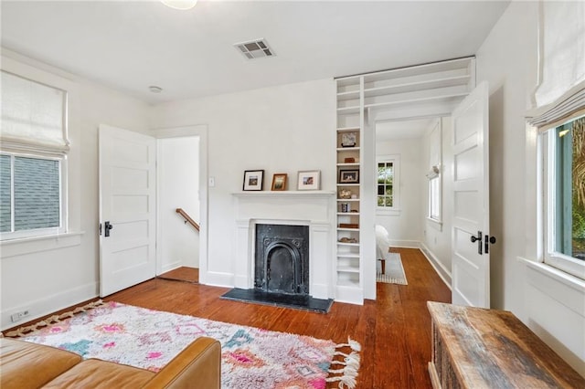 living room with a fireplace with raised hearth, dark wood-type flooring, a wealth of natural light, and visible vents