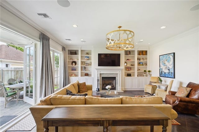 living room featuring built in features, visible vents, a high end fireplace, crown molding, and a notable chandelier