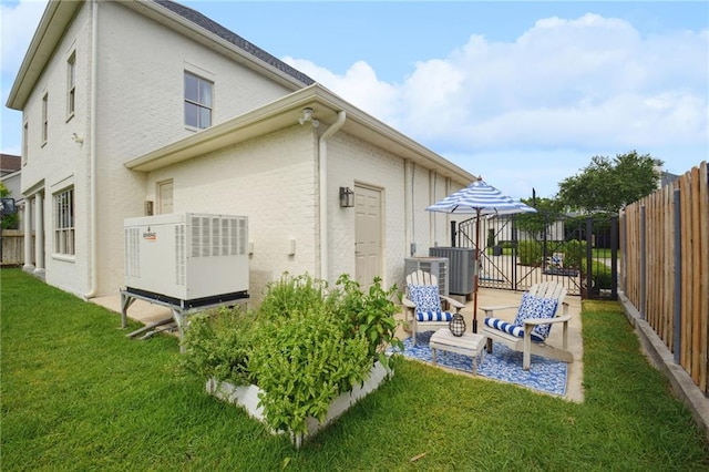 rear view of property featuring a patio, central AC unit, fence, a yard, and stucco siding