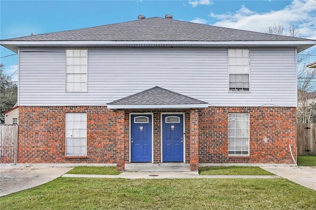 traditional-style house featuring roof with shingles, brick siding, a front lawn, and fence