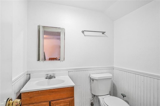 bathroom featuring toilet, vanity, vaulted ceiling, and wainscoting