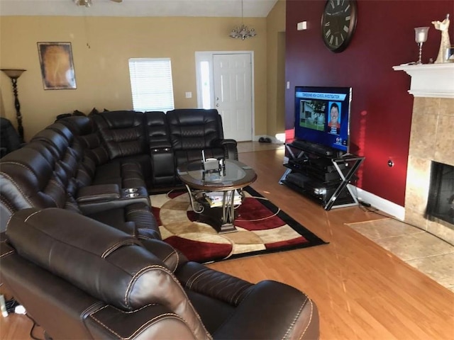 living area with lofted ceiling, a tiled fireplace, wood finished floors, and baseboards