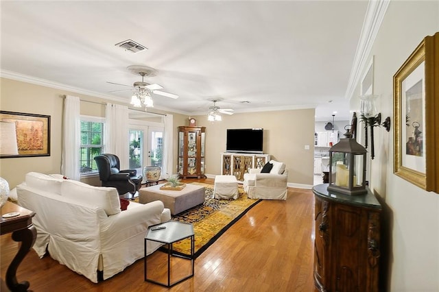 living area with wood finished floors, visible vents, french doors, and ornamental molding