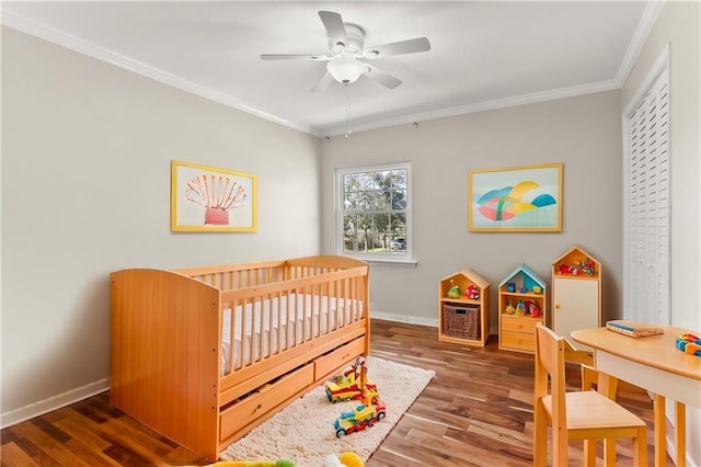 bedroom featuring ceiling fan, wood finished floors, baseboards, ornamental molding, and a nursery area