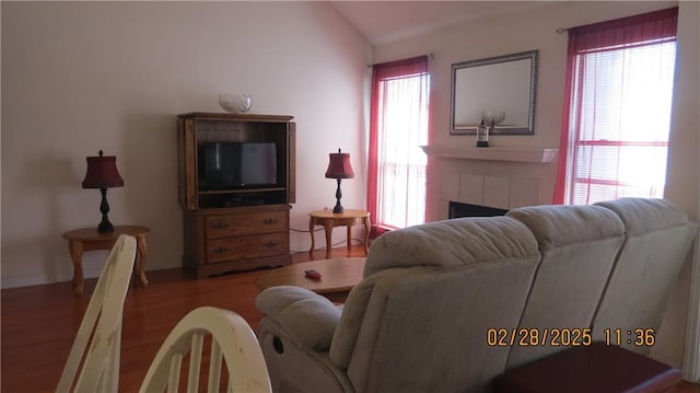 living room featuring lofted ceiling, a tiled fireplace, and wood finished floors