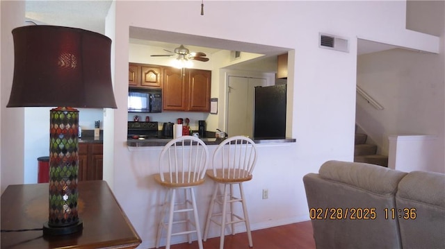 kitchen with visible vents, a breakfast bar area, brown cabinets, refrigerator, and black microwave