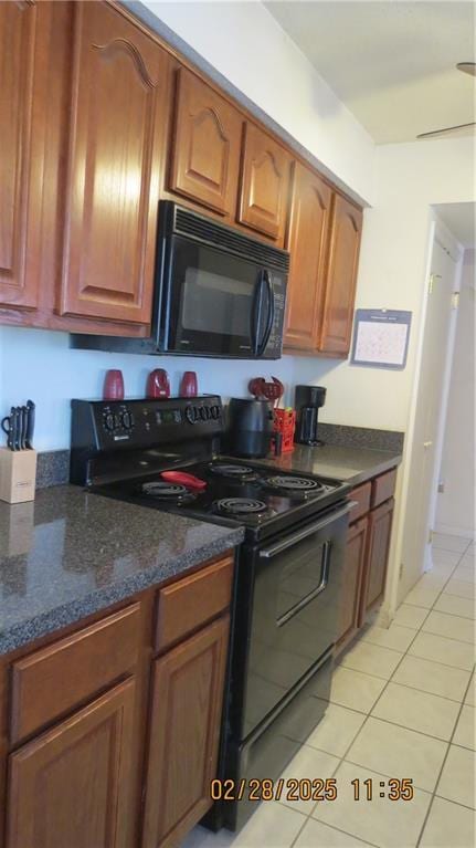 kitchen featuring dark stone counters, brown cabinets, black appliances, and light tile patterned floors