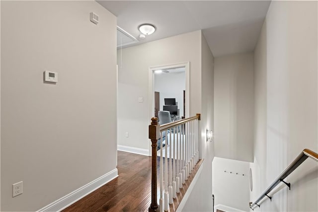 hallway featuring attic access, baseboards, dark wood finished floors, and an upstairs landing