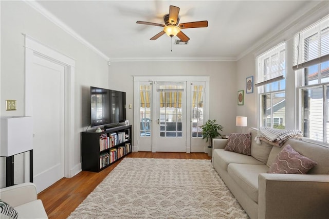 living area with a ceiling fan, visible vents, ornamental molding, and wood finished floors