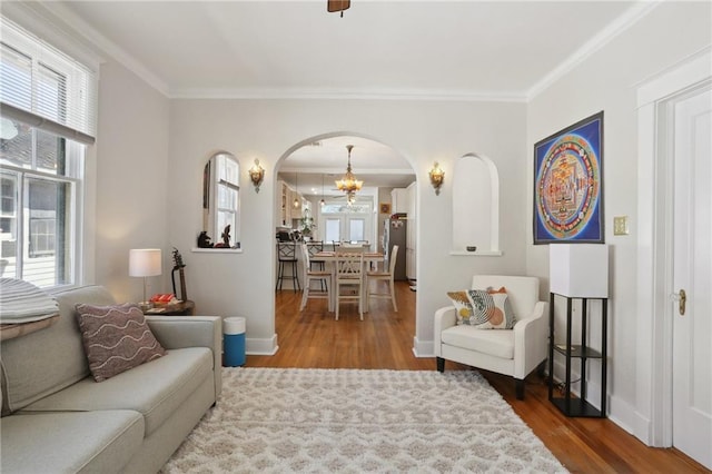 living area with a healthy amount of sunlight, arched walkways, wood finished floors, and ornamental molding