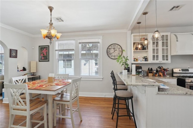 dining area with arched walkways, wood finished floors, visible vents, and crown molding