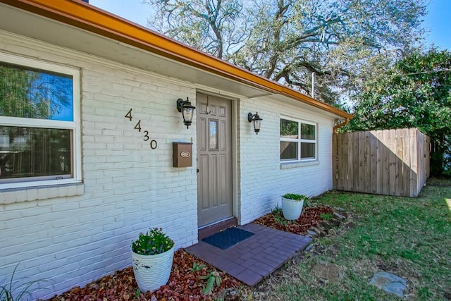 view of exterior entry featuring brick siding and fence