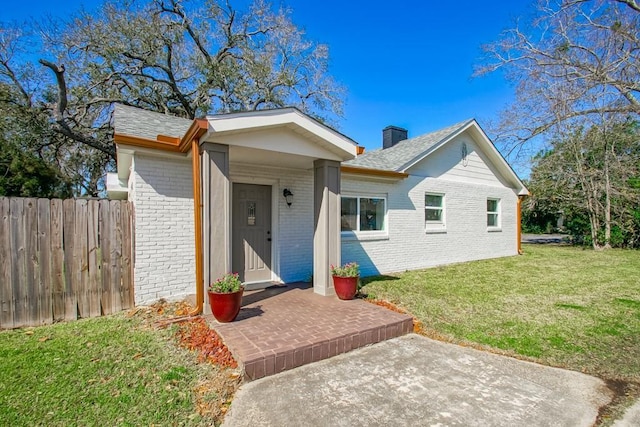 single story home with brick siding, fence, a chimney, and a front lawn