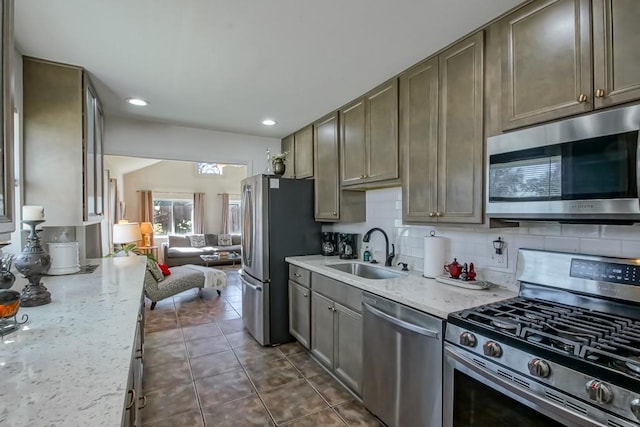 kitchen featuring light stone counters, stainless steel appliances, tasteful backsplash, a sink, and dark tile patterned floors